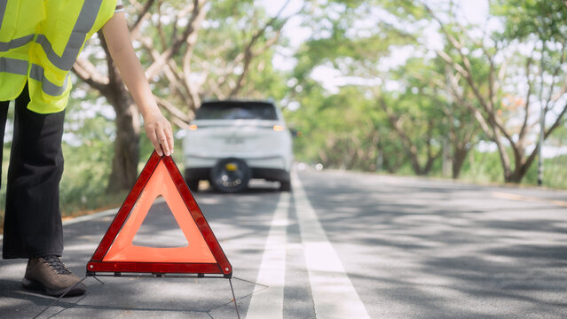 Person places warning sign on road after car issue in rural area during day