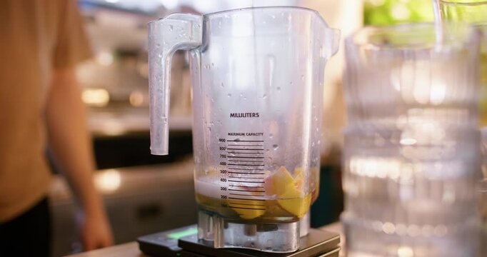 Preparing smoothie. Drink mixing. Bartender pouring alcohol liquid from bottle in blender measuring scale pitcher with fruit pieces.