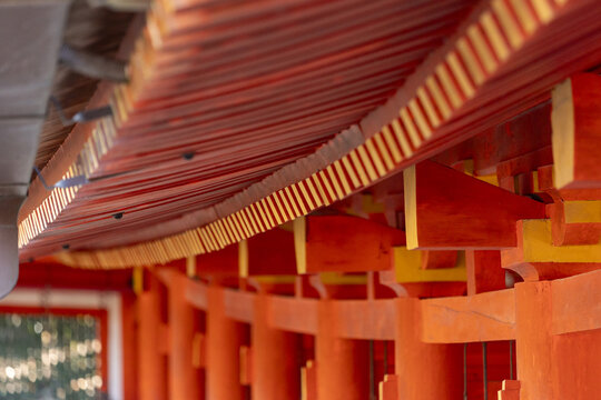 View of the intricate vermilion eaves and repetitive wooden pillars of a traditional Japanese shrine under soft daylight Nara, Nara, Japan.