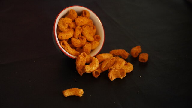Spicy Corn Puff Snacks Spilling from Bowl on Dark Background