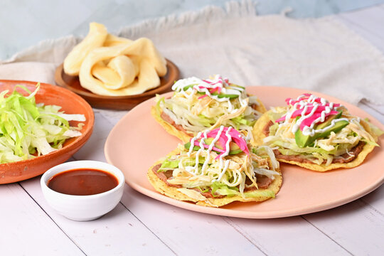 Authentic Mexican food concept. Delicious homemade tostadas with fresh ingredients, quesillo, lettuce and red salsa on the side