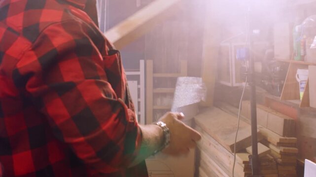 Joinery production Furniture making. Handyman putting on protective earmuffs processing wood on thickness planer in light interior.
