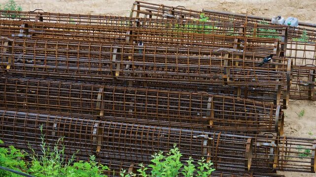 Magpies jump on rusty reinforced steel pile frames at a construction site. Birds hop between bored pile reinforcement cages outdoors in an industrial area. Close-up of foundation building materials.