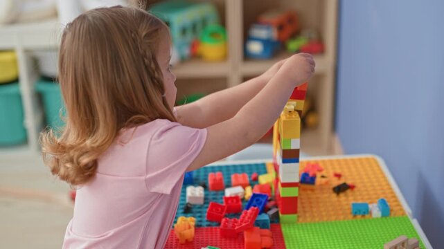 Little girl stacking colorful toy blocks with bare hands on a play table in a building; imaginative concentration.