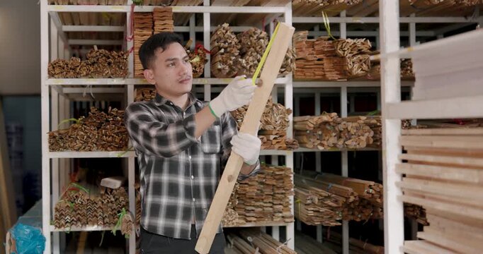 Asian adult man woodworking business owner measures vertical wooden board height using tape measure while verifying material dimensions for interior renovation wood inventory management