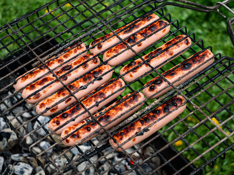 Appetizing sausages are placed in rows on the grill and grilled over coals. Close-up. Sausages on the grill on a background of grass and barbecue with coal.