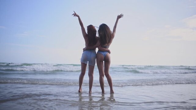 Women in stylish swimwear standing on sunny beach under clear blue sky adjusting their hair and enjoying carefree summer moment concepts of friendship vacation and tropical leisure.