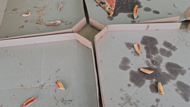 Pizza boxes after a party with leftover crusts and crumbs around the table in a messy layout during evening hours