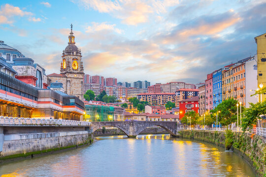 The historic Ribera Market and colorful waterfront buildings reflected in the Nervion River, Bilbao, Spain.