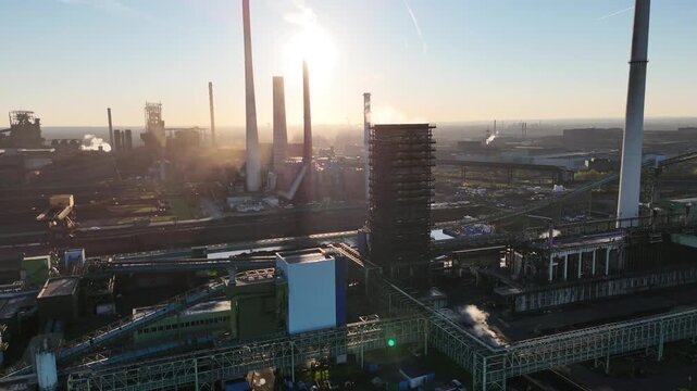 Drone move along the industrial riverfront with sun games and shifting smokestack shadows across frame
