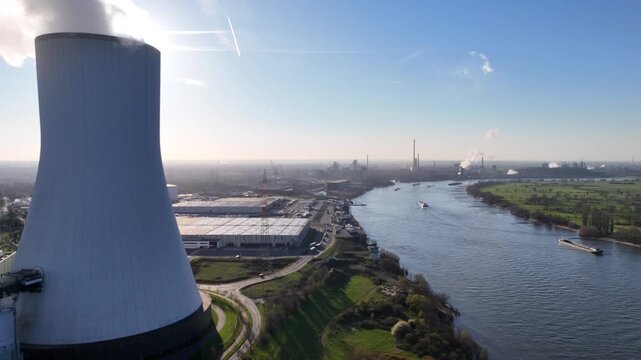 Drone crosses riverside grassland with cooling tower coking plant and the Rhine in one layered composition