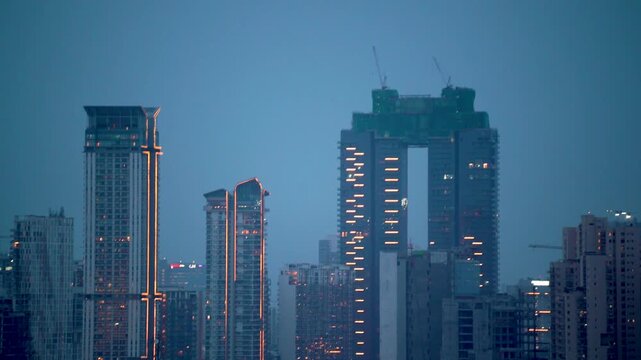 Aerial drone zoomed panning shot showing cityscape skyscrapers under construction buildings at night in mumbai hyderabad bangalore at blue hour with construction cranes and lights