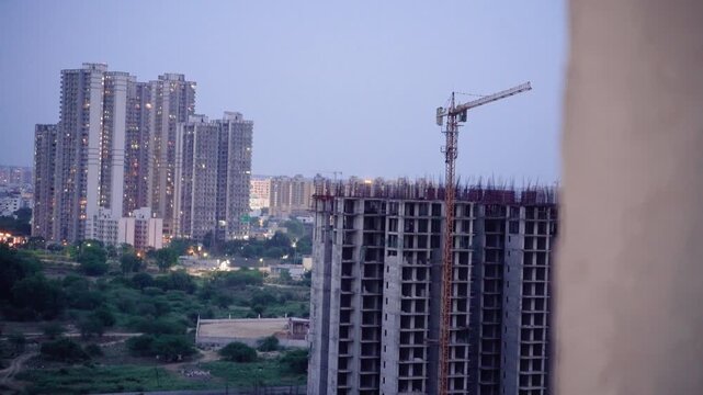 Slow pan reveal of under construction building with multi storey skyscraper in distance at dusk showing rapid real estate development in delhi gurgaon