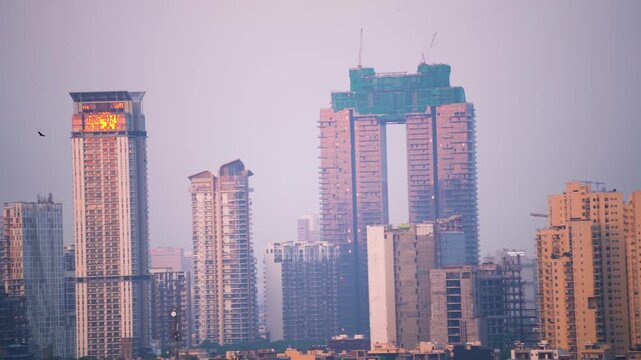 Aerial drone panning shot showing high rise skyscrapers under construction and completed cityscape of gurgaon delhi noida at dusk with sunlight reflected