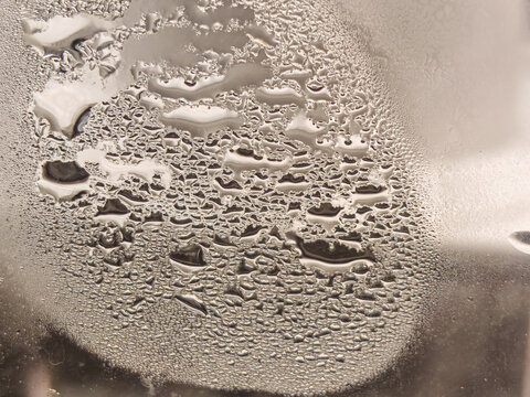 clear water condensation droplets and organic moisture patterns on a glass surface reflecting warm metallic light