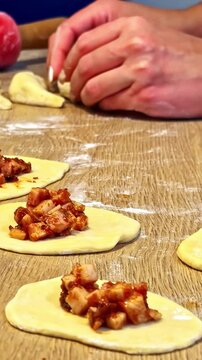 Hand shaping dough pastry filled with savory meat stuffing on a floured wooden workspace table - vertical closeup shot