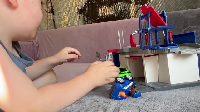 child playing with toys, a young boy focuses on playing with colorful toy cars and a multi-level garage playset on a grey surface.