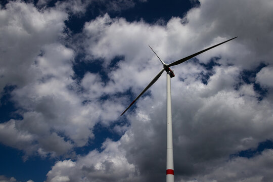 View of a tall wind turbine with red stripes on the blades and mast against a dramatic cloudy sky Germany.