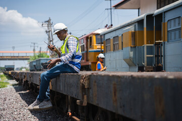 Fototapeta premium Railway logistics supervisor communicating via walkie talkie at freight train terminal, Engineer checking cargo transport operations, Worker sitting on freight wagon using portable radio communication