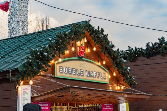 VDNH exhibition center in Kyiv, public festivity, mulled wine for sale, food stall named Bubble Waffle, Christmas decorations, shades of brown, green, white, red acc