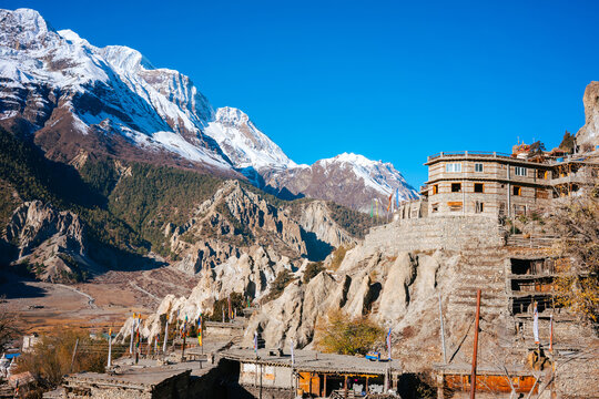 The ancient village of Manang clings to rocky cliffs with a Buddhist gompa and prayer flags beneath the snow-capped Annapurna massif.