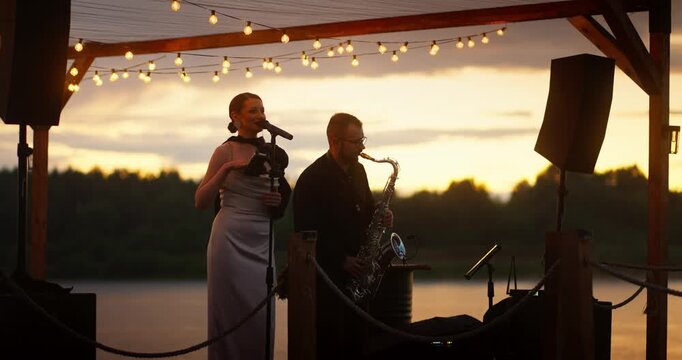 Lakeside duet at sunset on wooden pavilion with string lights