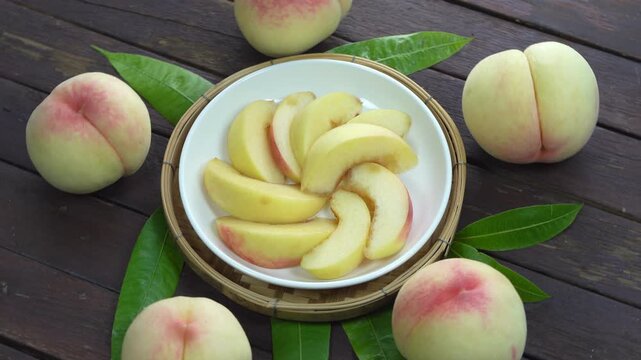 White Peaches with leaves and Slice of  Peach on white dish, Fresh White Peach on wooden basket in wooden Background.