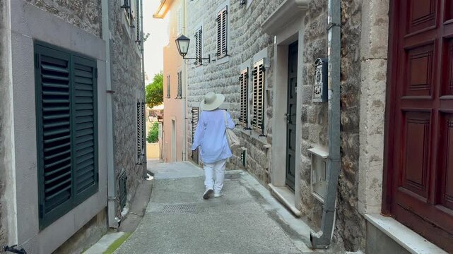 Senior Woman Walking Through Mediterranean Old Town. Senior female tourist walking along a narrow street in a historic Mediterranean town. Independent travel, sightseeing and active retirement. 