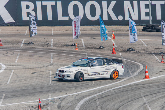 White BMW sports car with blue and orange stripes, mid-drift on a racing track with multiple lanes, late afternoonevening lighting, natural environment, BITRACK eve - Kyiv, Ukraine 06-15-2025