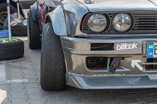 Vintage BMW car, silver-gray with black side stripe, low profile, daytime outdoor setting, possibly at a show or exhibition, UA 360 license plate, Batmobile decal, n - Kyiv, Ukraine 06-15-2025