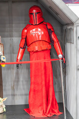Naklejka premium Life-sized Star Wars costume figure in red armor, against a dark backdrop Red cape, helmet with visor, chest piece adorned with symbols, articulated arm sections, b - Kyiv, Ukraine - June 7, 2025