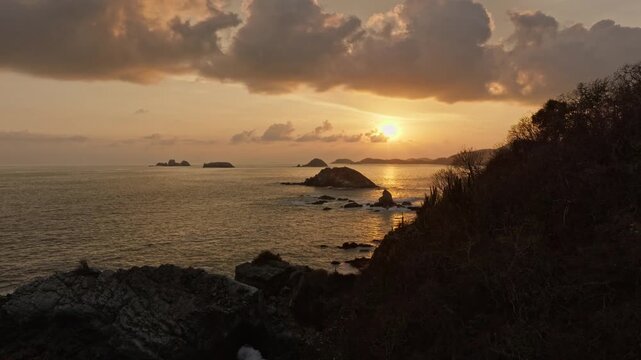 Golden sunset over rocky islands and calm ocean waters near the Zihuatanejo coast, aerial ascend