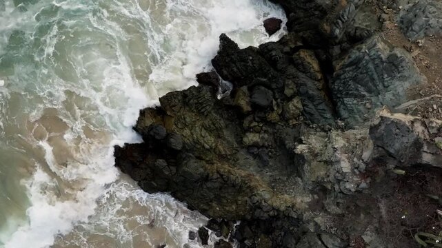 Aerial backdrop of rugged coastal rock formations and crashing surf in Zihuatanejo, drone establishing background, ascend