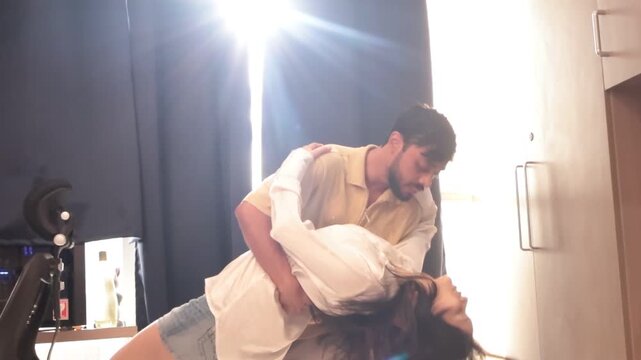 Young couple dancing together in sunlit room with bright morning light streaming through curtains