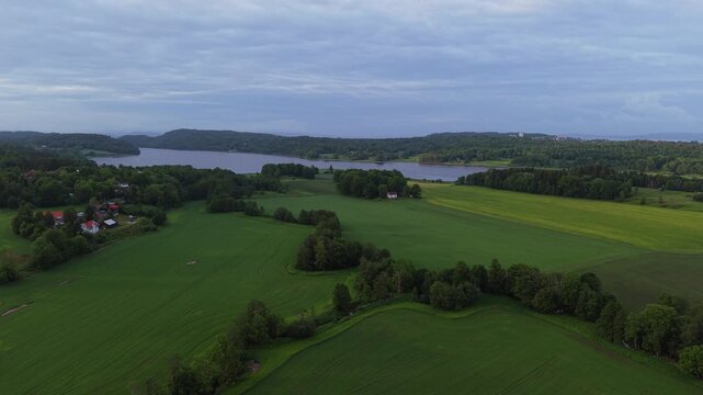 Lush green fields stretching to a distant lake under a cloudy sky. Ideal for landscape documentaries or travel features highlighting Norway's countryside.
