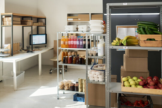 Wide shot of order pickup point storing fresh produce, packaged meals, bottled drinks and shipping boxes near workstation. Suitable for grocery delivery, fulfillment, retail logistics marketing