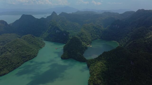 Cinematic 4K slow motion drone shot of the pristine green waters of Dayang Bunting Lake, surrounded by tropical limestone mountains in Langkawi, Malaysia.