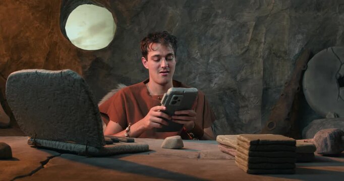 Funny Caveman Using Stone Smartphone and Expressing Joy in Prehistoric Cave