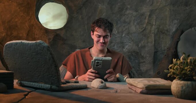 Funny Caveman Checking Stone Smartwatch and Working on Laptop in Prehistoric Cave