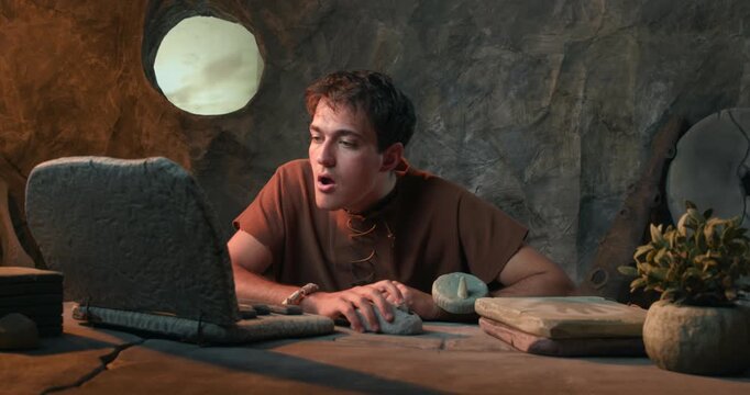Funny Caveman Using Stone Mouse and Working on Laptop in Prehistoric Cave