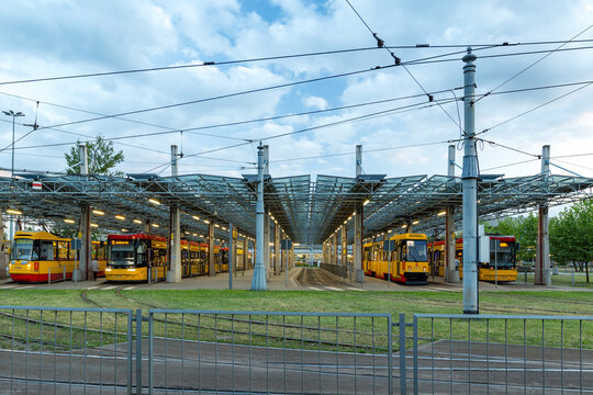 View of yellow and red trams parked at a modern station under a metal canopy with overhead electric lines Warsaw, Masovian Voivodeship, Poland.