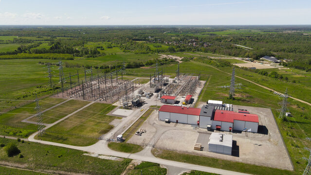 Aerial view of a modern data center and adjacent electrical substation in a green rural landscape, showing transmission lines, transformers and solar ready infrastructure