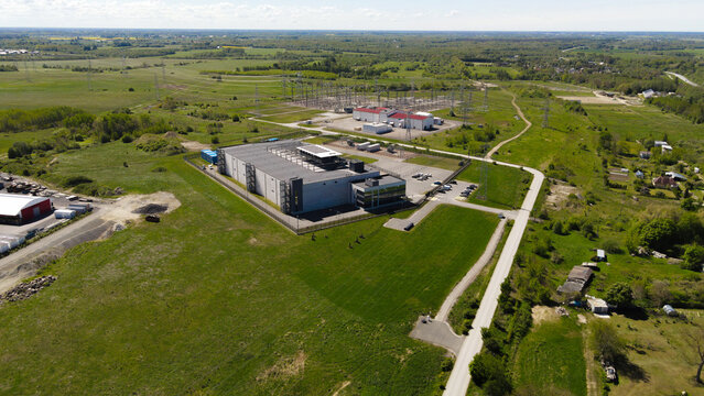 Aerial view showing a large hyperscale data center building and an interconnected high voltage electrical substation providing power, set within a green rural landscape
