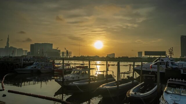 Beautiful golden sunrise timelapse over Saigon river pier with speedboats and city skyline background.