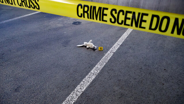Yellow crime scene tape marking off an area on asphalt pavement with a small, dirty toy bunny and an evidence marker, conveying themes of loss, tragedy, and investigation