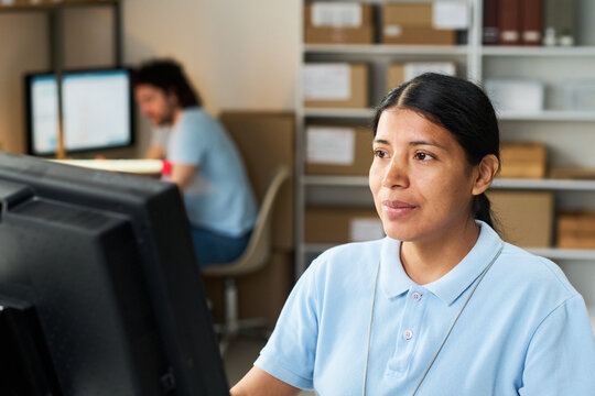 Asian young woman processing pickup orders at service desk while coworker managing deliveries in background. Ideal for logistics, retail fulfillment, customer service marketing