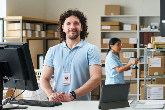 Portrait of young man standing at order pickup counter while Asian woman scanning parcels in fulfillment room. Ideal for delivery service, retail logistics marketing