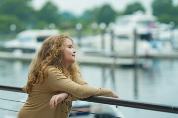 Obraz premium Teenager portrait by harbor. Teenager looking away outdoors. Teenager leaning near marina. Teenager with blurred boats.