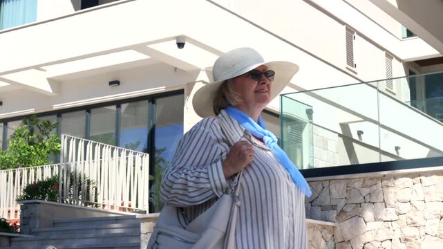 Mature Woman Enjoying Summer Travel in Europe. Mature female tourist walking outdoors near a modern Mediterranean building in summer. Active retirement, independent travel and senior lifestyle concept