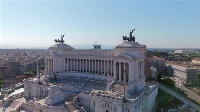 Aerial drone footage captures stunning Vittoriano monument in Rome's Piazza Venezia, featuring white marble columns, bronze chariot statues atop towers.